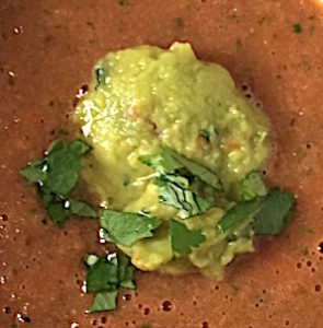 Guacamole and chopped cilantro enrich a cup of gazpacho